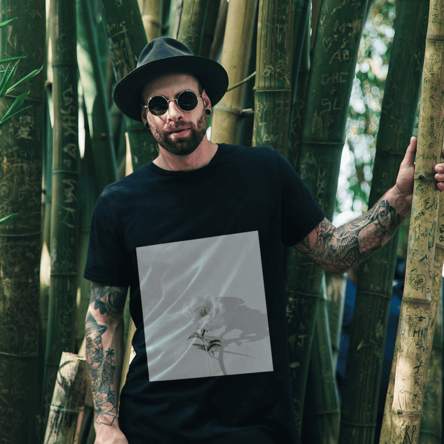 Man wearing a black t-shirt with a white rose graphic, standing among bamboo trees.
