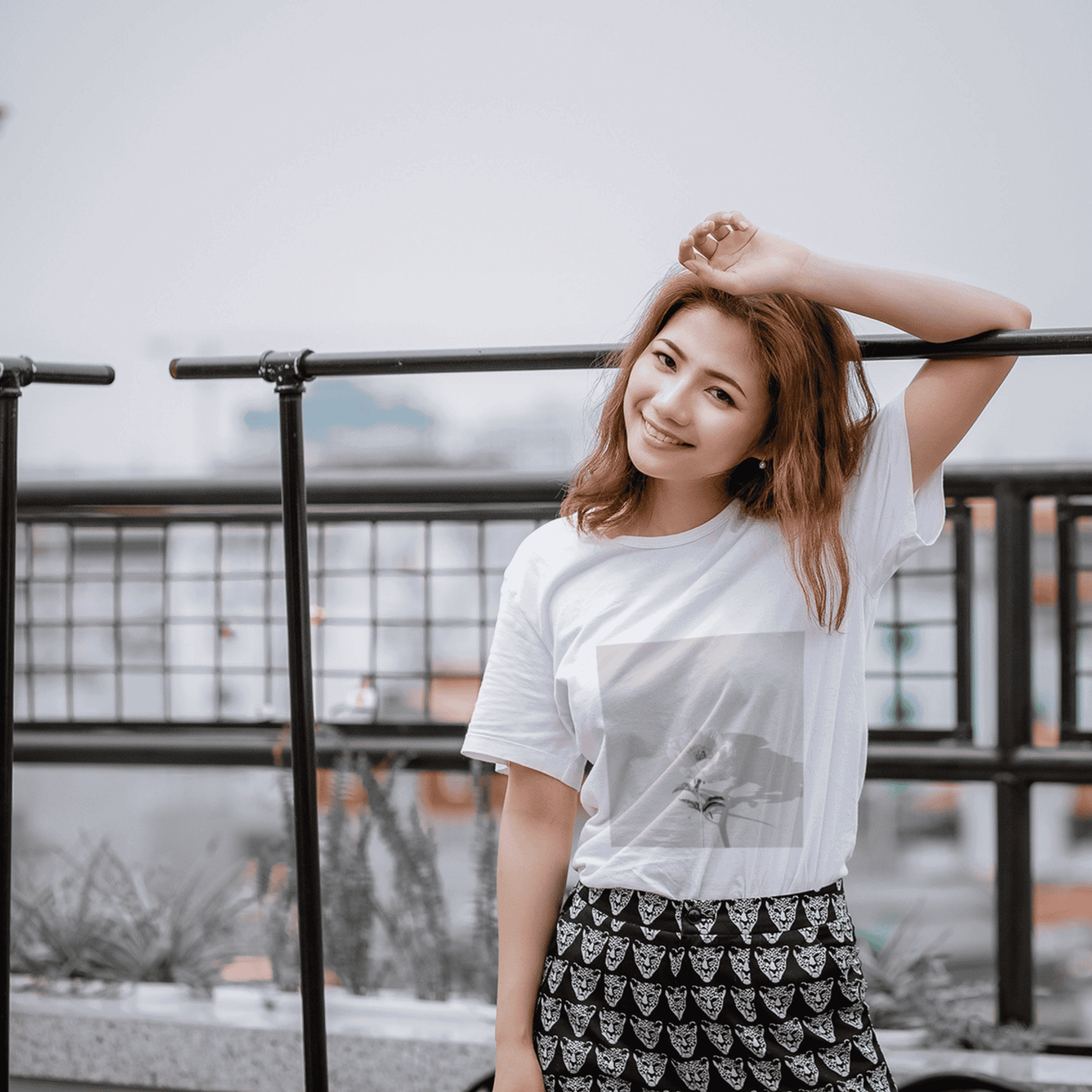 Young woman wearing a white t-shirt with flower photography on a city rooftop.
