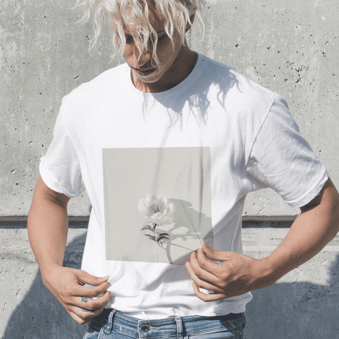 Man wearing a white t-shirt featuring a single white rose print, standing against a textured concrete wall.