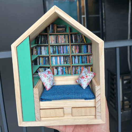 Miniature house-shaped bookshelf with tiny shelves, couch, and decorative pillows.