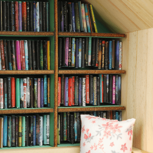 Close-up of a miniature bookshelf filled with colorful miniature anxiety books and a decorative pillow.