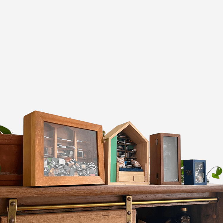 Four Piece Anxiety Bookshelf Collection displayed on a wooden shelf, featuring miniature bookshelves.