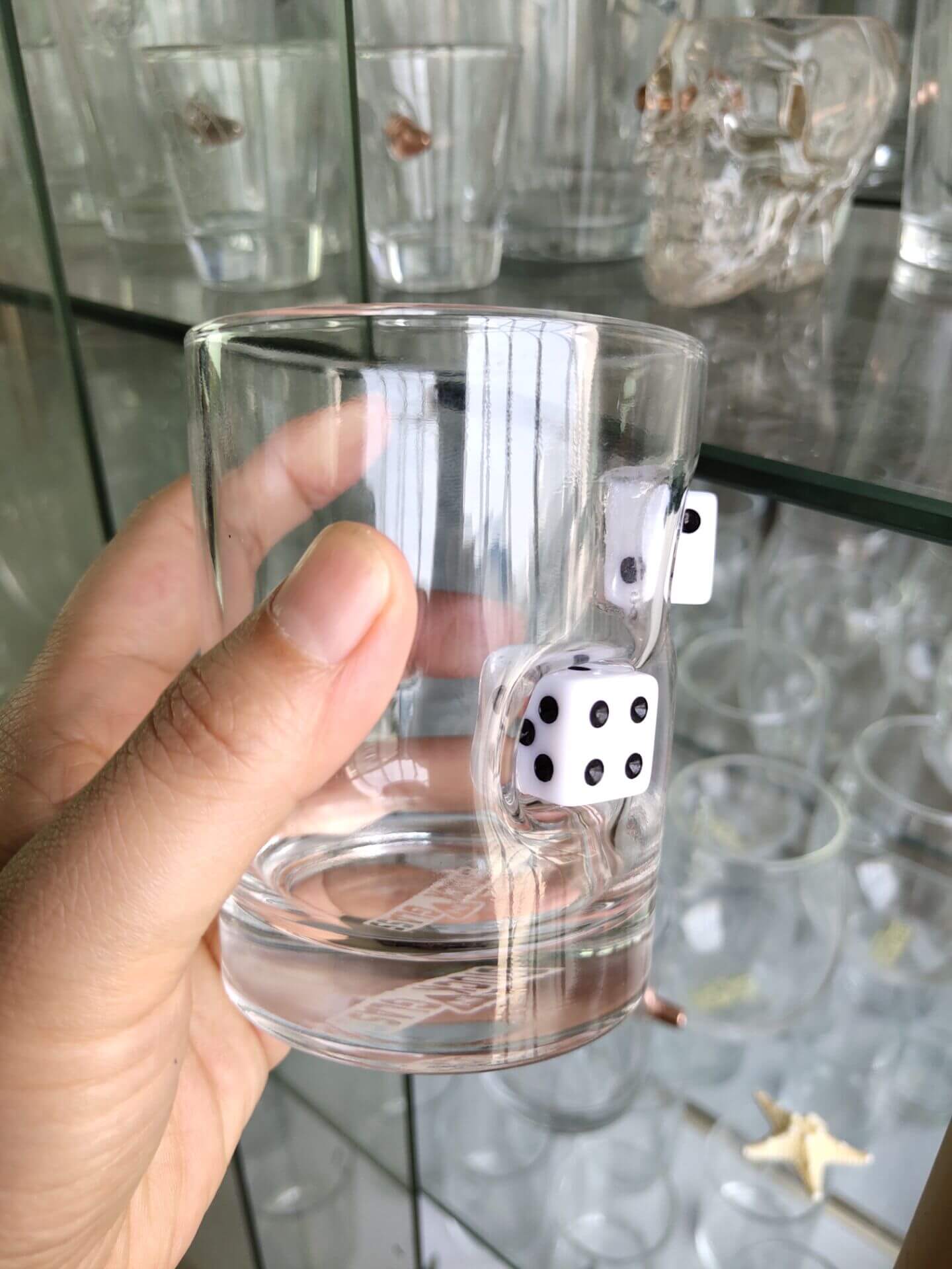 Hand holding a clear glass cup with embedded black-and-white dice, showcasing a unique whiskey glass design.