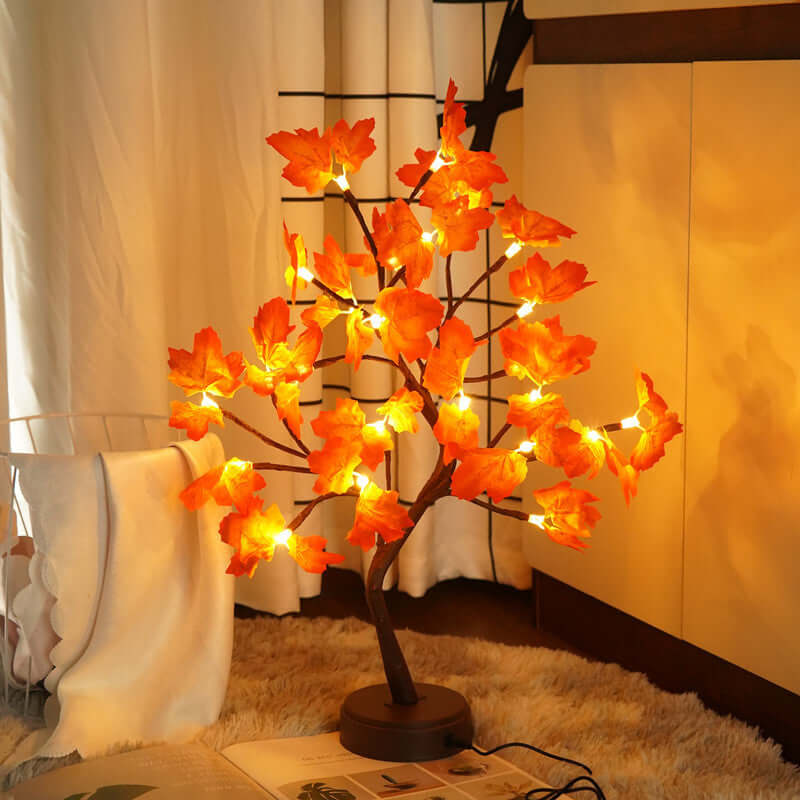 Lit wire tree sculpture with orange maple leaves, providing artistic ambiance for home decor.