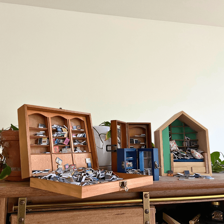 Miniature bookshelves collection showcasing various tiny books in unique designs on a wooden surface.