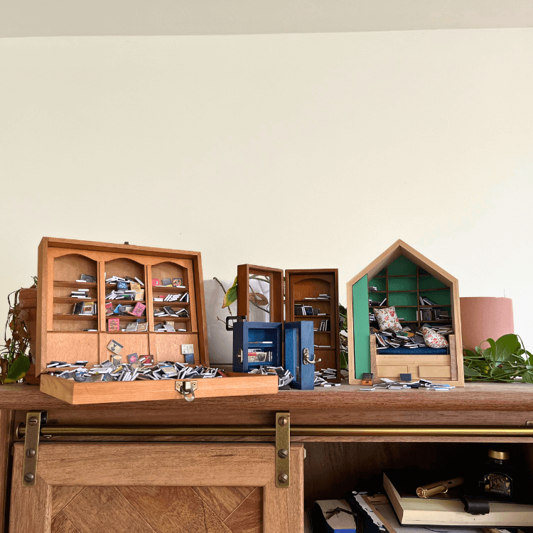 A collection of miniature bookshelves and shelves filled with tiny books and accessories on a wooden surface.