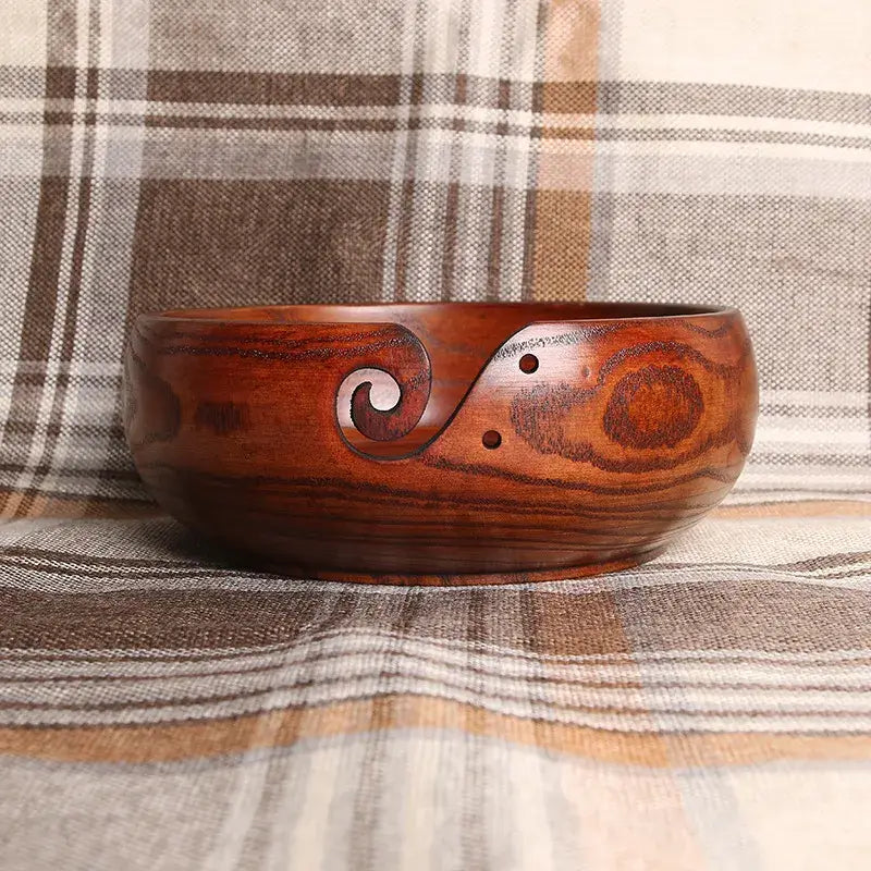 Handmade wooden crochet yarn bowl with decorative carving on a plaid background.