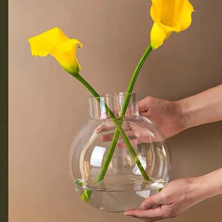 Clear glass vase with two yellow flowers being held against a neutral background.