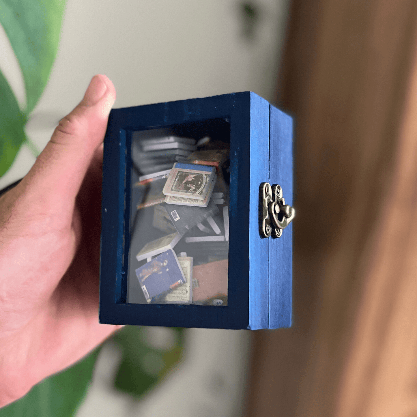 Hand holding a blue miniature bookshelf filled with tiny books and curiosities.
