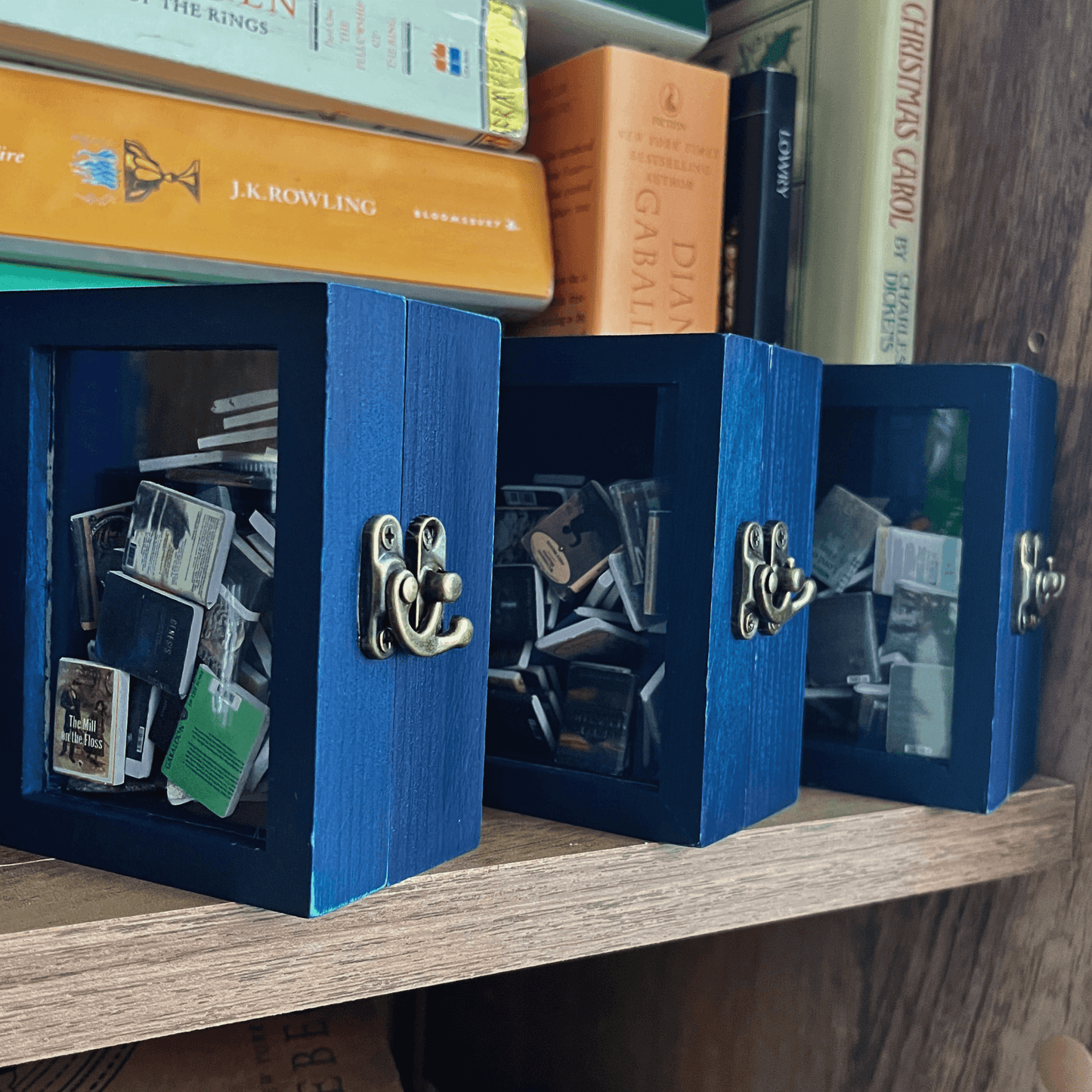 Three of the blue mini Pocket Anxiety Bookshelf are displayed with the best mini books. The bookshelf features an antique style latch.