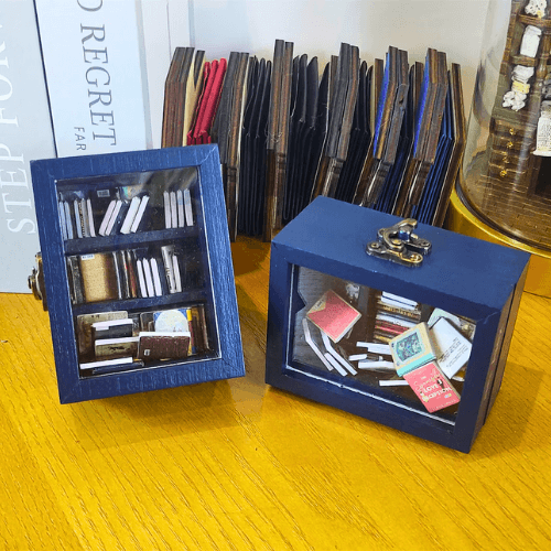 Two Pocket Anxiety Bookshelf mini bookshelves are shown. One is standing, and one on its side. The clear display case shows the miniature books inside.