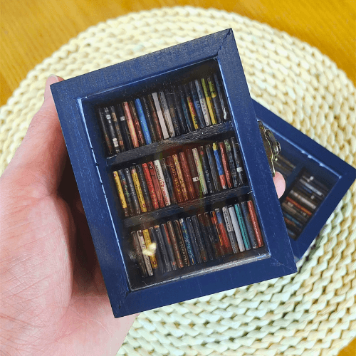 The Pocket Anxiety Bookshelf is held close to the camera for a close up view of the tardis blue paint and miniature books.