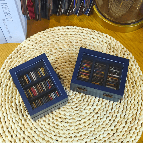 Two Mini Blue Pocket Anxiety Bookshelves are imaged sitting on a circular beige placemat.