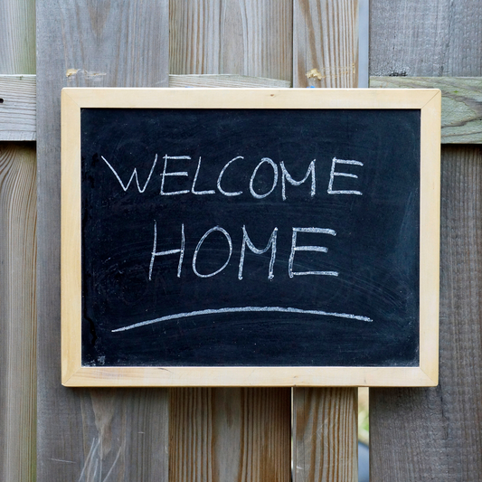 Welcome home sign hangs on a wood fence.