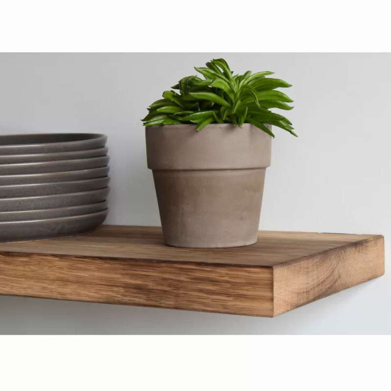 A solid burnt oak floating shelf is displayed with a potted succulent and a stack of plates.