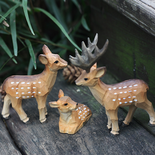 Hand carved deer figurines sit in a rustic setting on a distressed wood table.