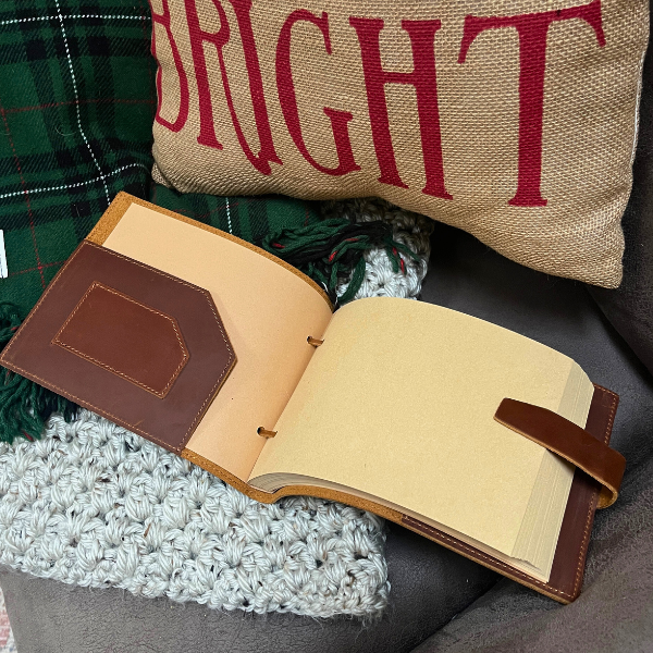 Landscape oriented leather sketchbook sits open on a holiday themed chair.