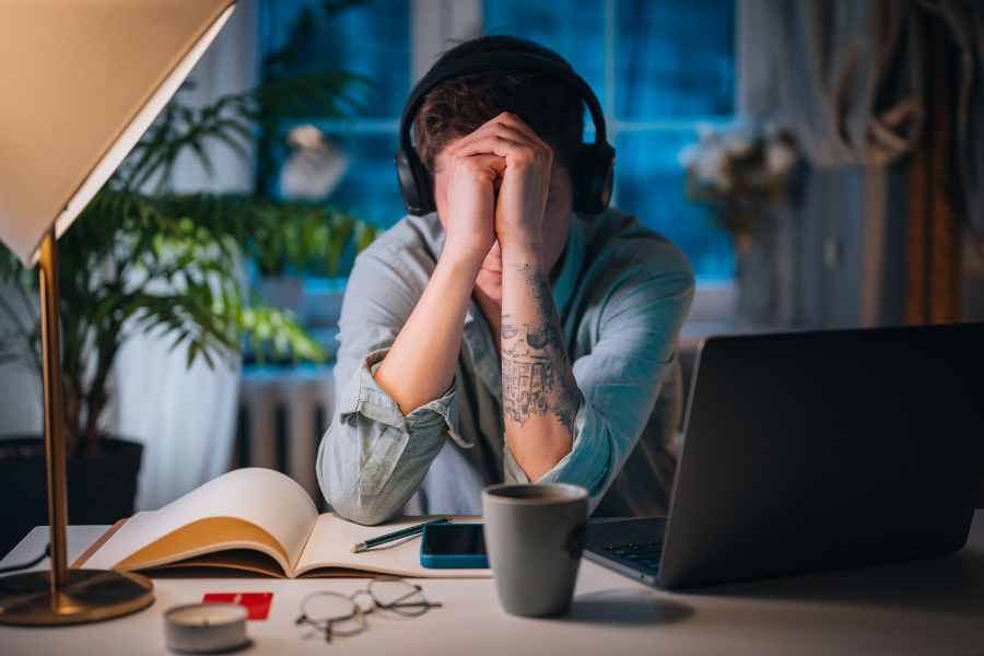 A woman sits at her desk with hands over her face, signifying anxiety and sadness.