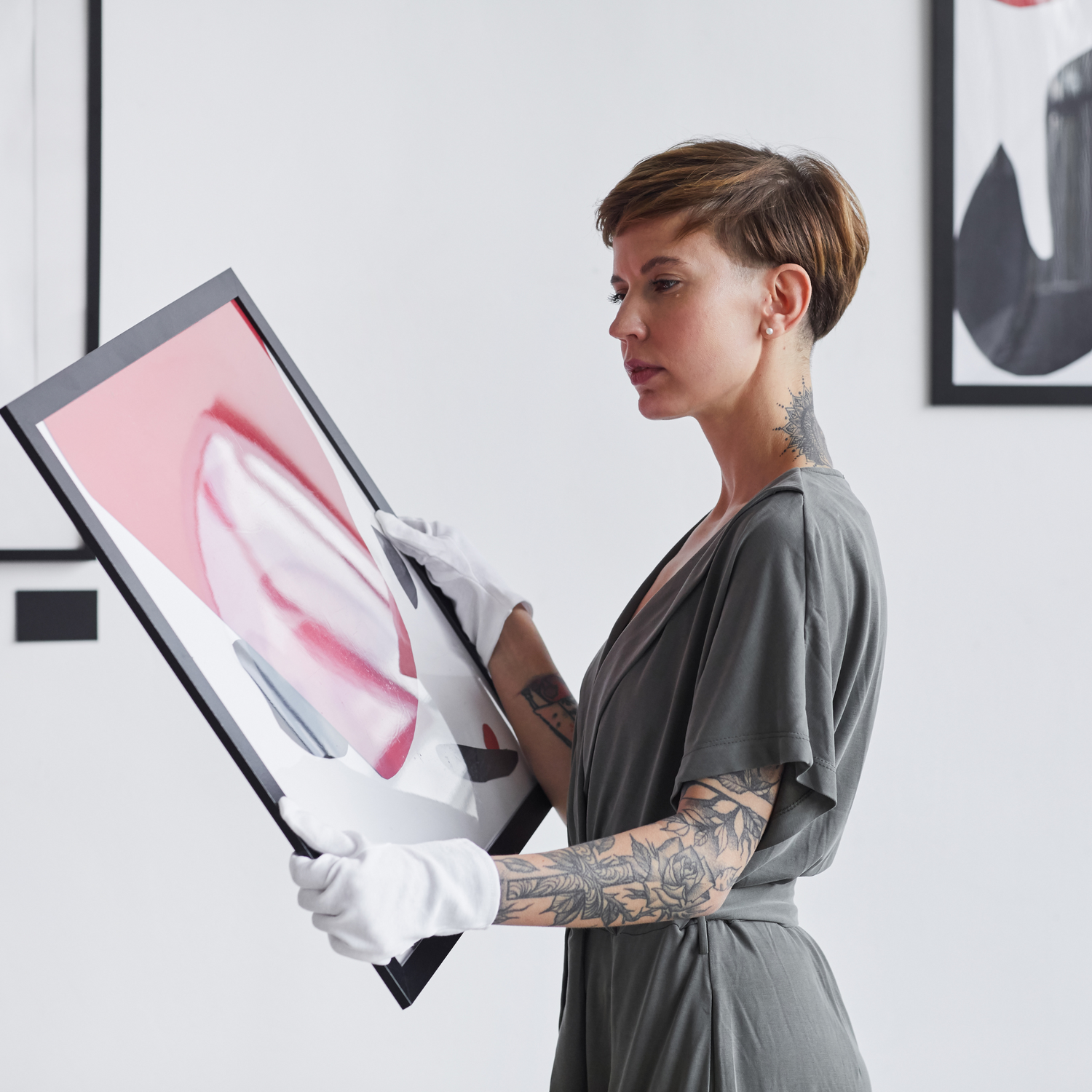 An attractive woman with tattoos wearing white gloves and holding while admiring a painting.