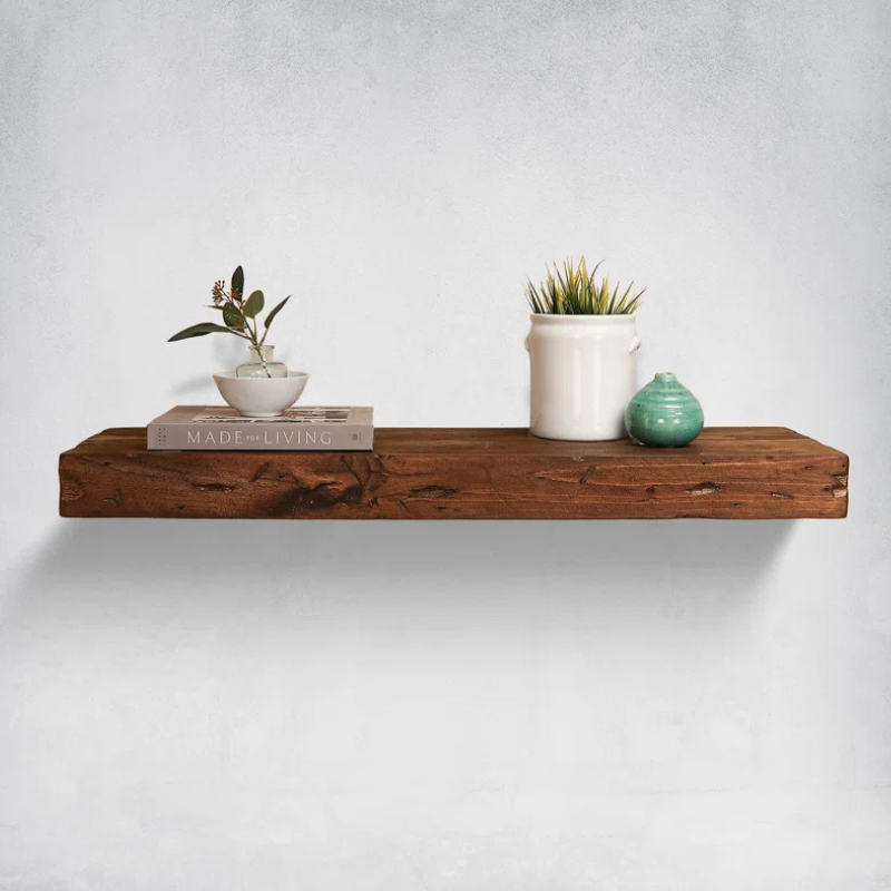 A hand distressed floating shelf with a succulent and decor. The shelf has a natural dark wood grain finish and sits against a light grey wall to highlight its hidden, floating look.