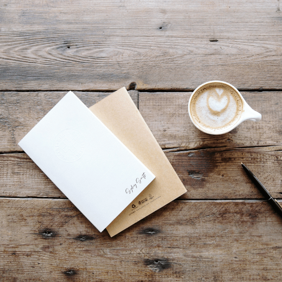 a blank card sits on a wooden table beside an espresso and a pen with it's cap removed