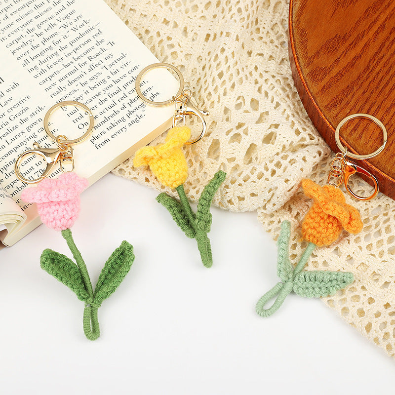 Handmade crochet flower keychains in pink, yellow, and orange, featuring stems, displayed on a vintage book and fabric.