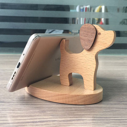 Wood animal shaped phone stand in the form of a dog holding a smartphone upright on a wooden base.