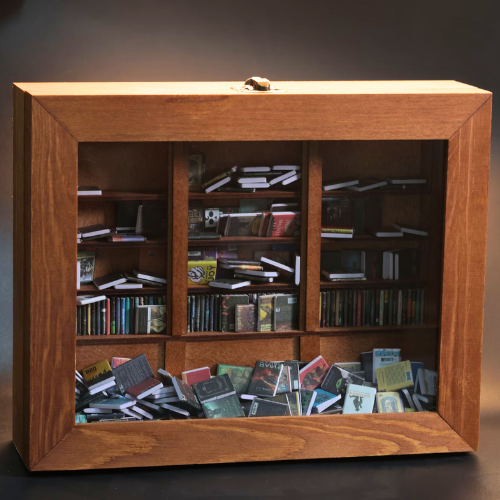 The Anxiety Bookshelf sits on top of a real bookshelf. The mini bookshelf is filled with miniature replica books. It is a shakeable book box that you organize, stack, and shake to reduce stress and anxiety.