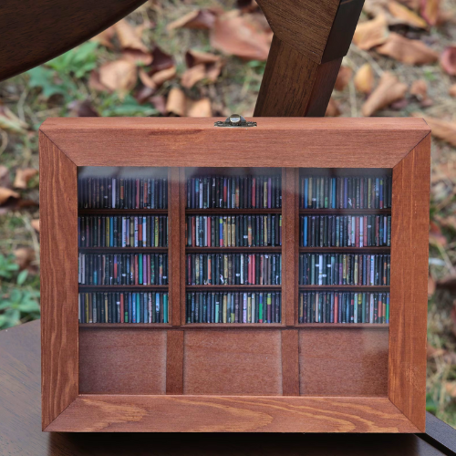 The Anxiety Bookshelf sits on a chair outdoors in fall with leaves around. The mini bookshelf is filled with miniature replica books. It is a shakeable book box that you organize, stack, and shake to reduce stress and anxiety.