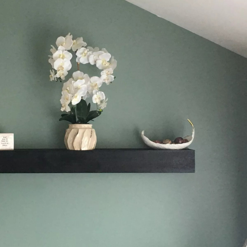 Black stained mantel slipcover sits on a green wall.