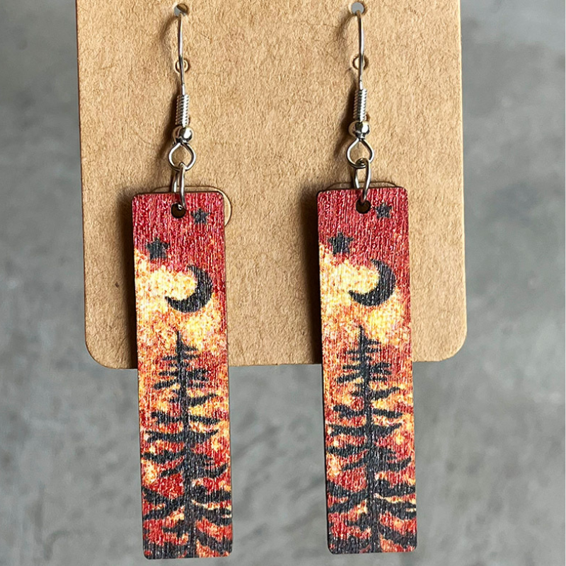 Wood mini bookmark earrings with black moon, star and pine tree silhouettes over a watercolour background.