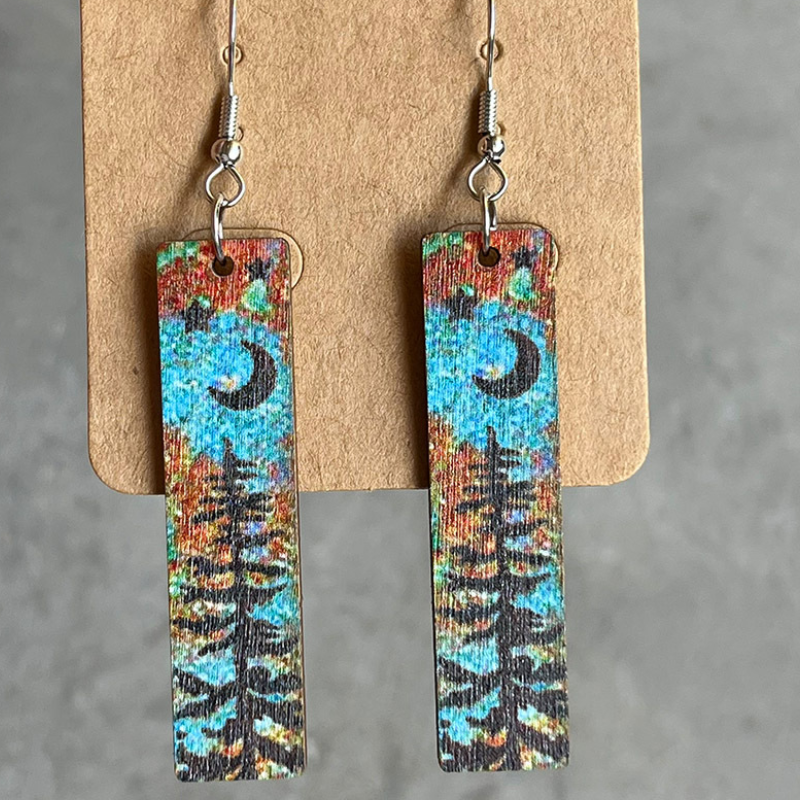 Wood mini bookmark earrings with black moon, star and pine tree silhouettes over a watercolour background.