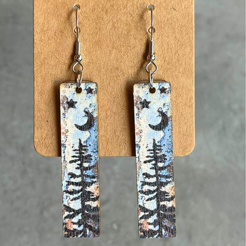 Wood mini bookmark earrings with black moon, star and pine tree silhouettes over a watercolour background.