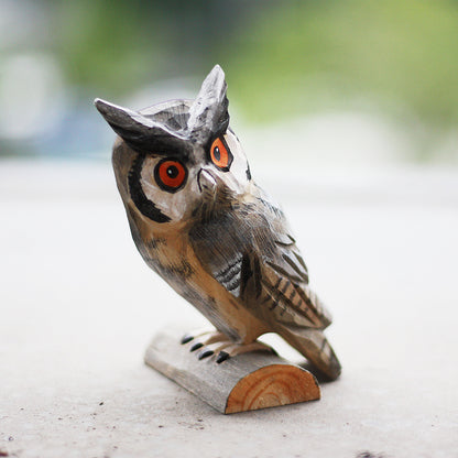 Hand carved long eared owl ornament sits perched on a small wood log.