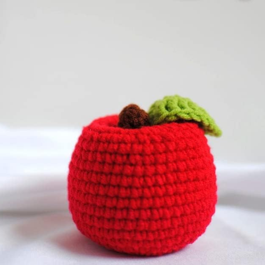 Handmade crochet red apple plushie is displayed over a white background.