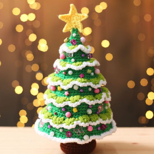 Handmade crochet christmas tree plushie is displayed over a burry background with twinkling lights.