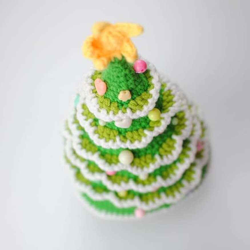 Handmade crochet christmas tree plushie is displayed from an overhead view highlighting the details and attached ornaments.