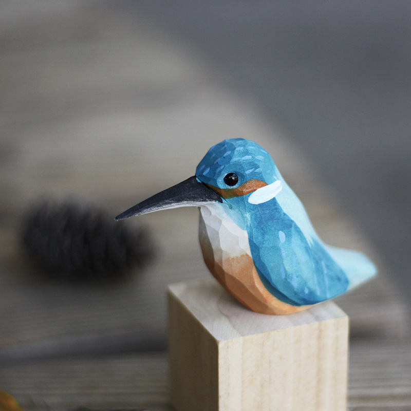 Hand carved bird ornaments sit on top of a wood block. Featured are the kingfisher, goldcrest, robin, and eurasian wren.