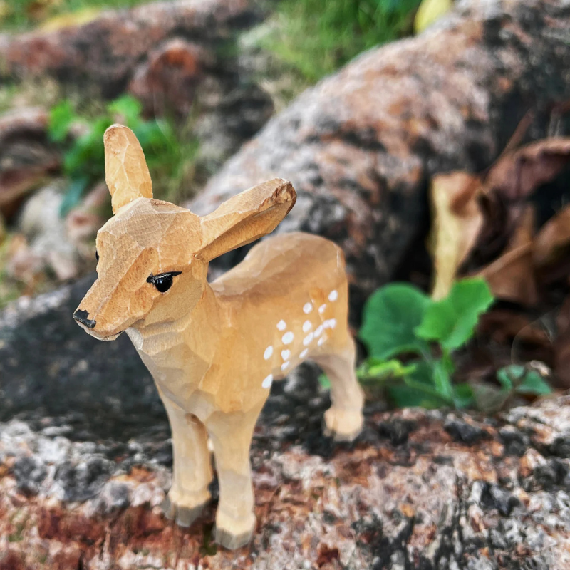 Hand-carved deer ornament showcasing natural wood textures in a natural setting.