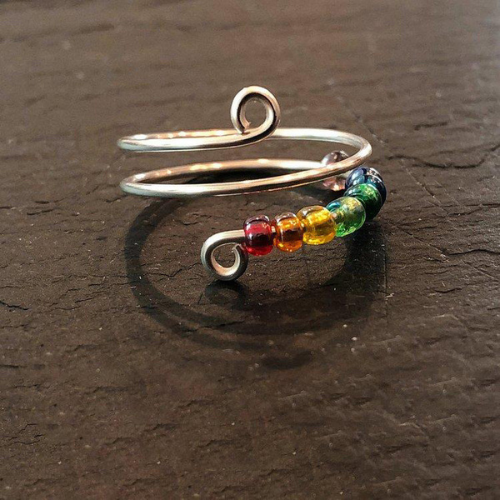 Spiral rainbow beaded fidget ring for anxiety sits on a table.