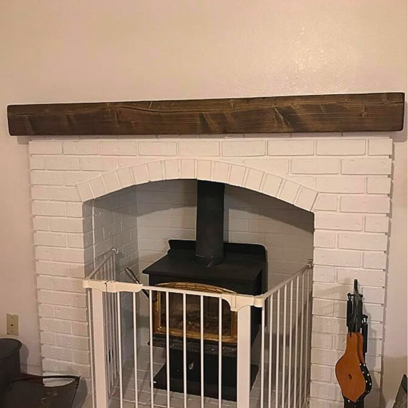 A solid 6x6 cedar wood-stained, lightly distressed floating mantel beam sits over a fireplace.