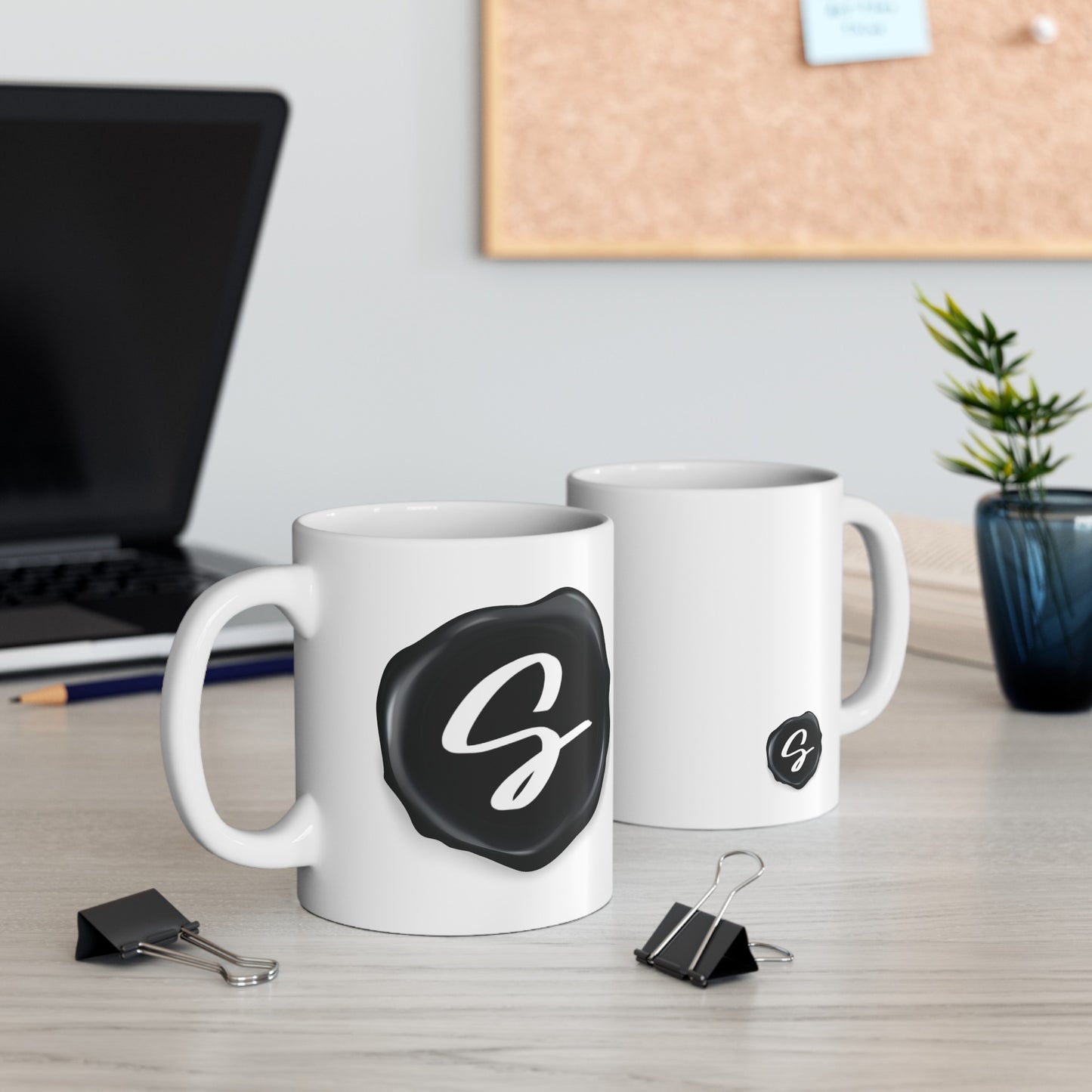 Sydney's Collection black wax seal logo is featured on a coffee mug, displayed as a pair as desk decor.