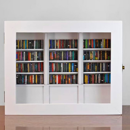 White Anxiety Bookshelf with books displayed as desk decor or bedroom decor. Some of the mini books are organized on the shelves, and some are disorganized on the tabletop. The white anxiety bookshelf is a miniature bookcase in a box with a door that opens to access the included miniature books.