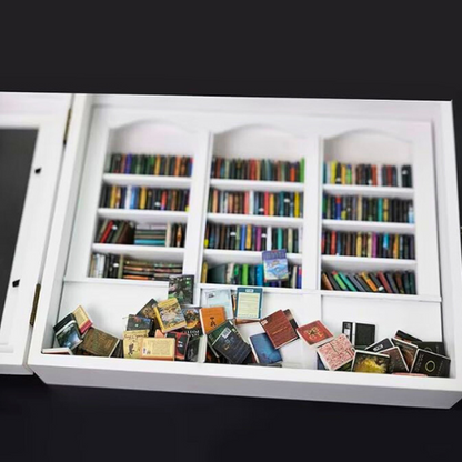 White Anxiety Bookshelf with books displayed as desk decor or bedroom decor. Some of the mini books are organized on the shelves, and some are disorganized on the tabletop. The white anxiety bookshelf is a miniature bookcase in a box with a door that opens to access the included miniature books.