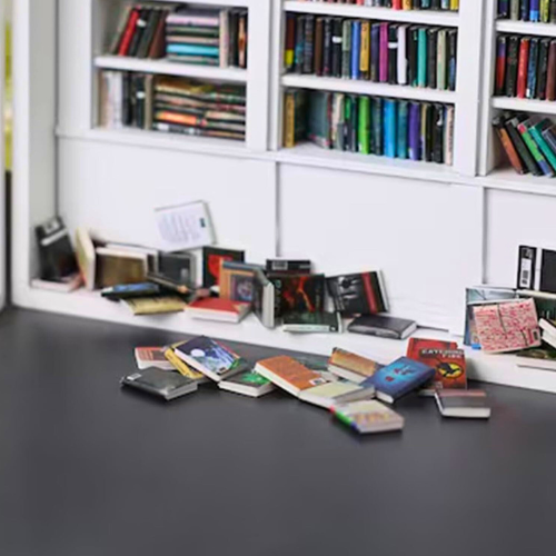 White Anxiety Bookshelf with books displayed as desk decor or bedroom decor. Some of the mini books are organized on the shelves, and some are disorganized on the tabletop. The white anxiety bookshelf is a miniature bookcase in a box with a door that opens to access the included miniature books.