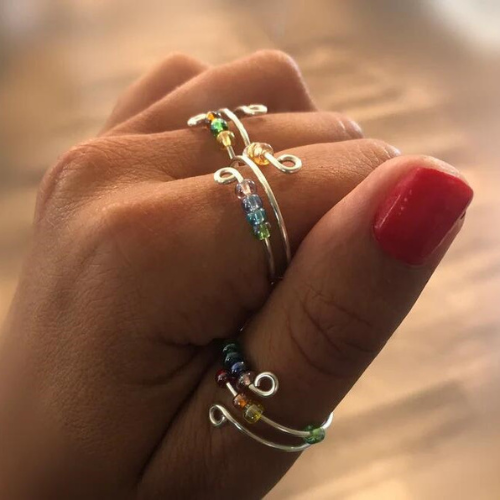 Beaded rainbow fidget rings for anxiety are displayed on a models hand.