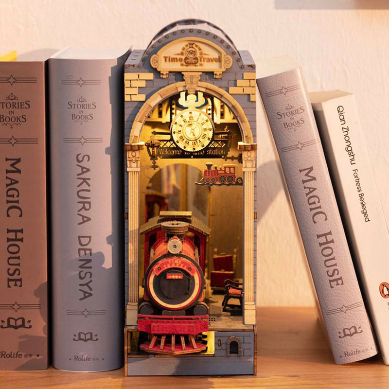 A train themed book nook nested between books, illuminated inside with its dim light.