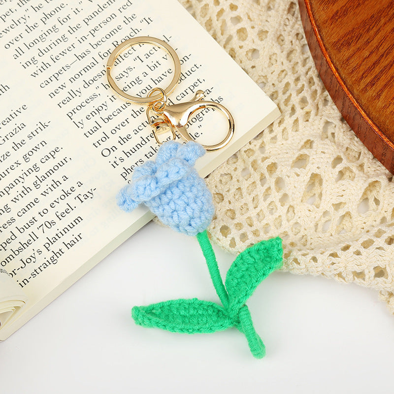 Handmade crochet flower keychain in blue with green stem next to an open book and lace fabric.