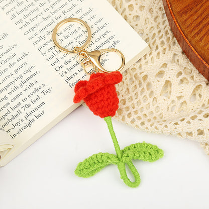 Handmade red crochet flower keychain with green stem, resting on a book and crochet lace.