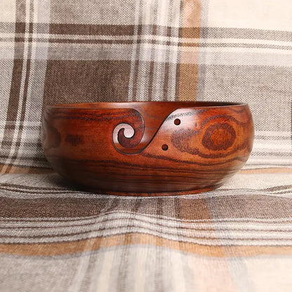 Handmade wooden crochet yarn bowl with decorative carving on a plaid background.